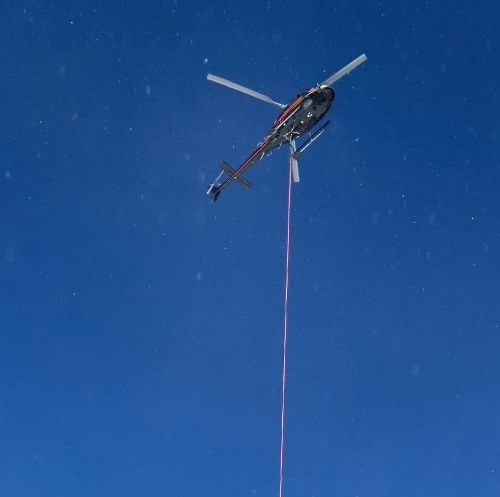 Helicopter hovers above US 160 Wolf Creek Pass with a suspension line used to place and remove avalanche mitigation equipment along the highway.