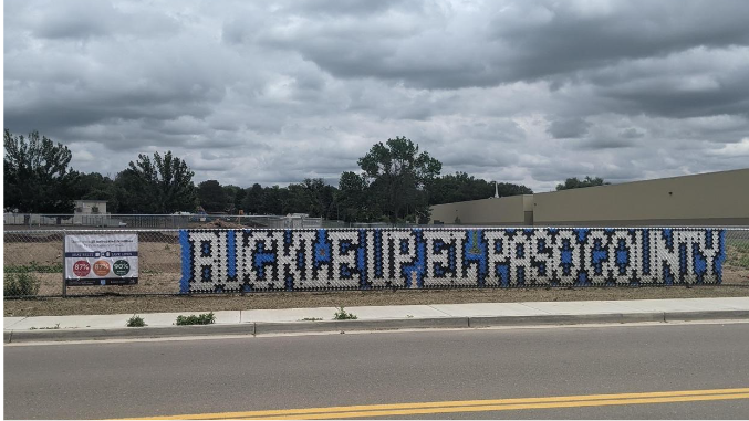 "Buckle up El Paso County" displayed on chain-link fence