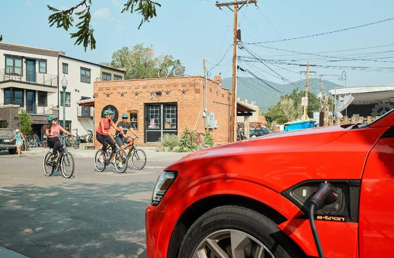 Red electric sedan charging on a residential street with bicycle rides in the background. 