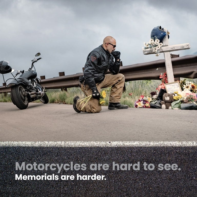 Motorcyclist kneeling next to a memorial next to the road